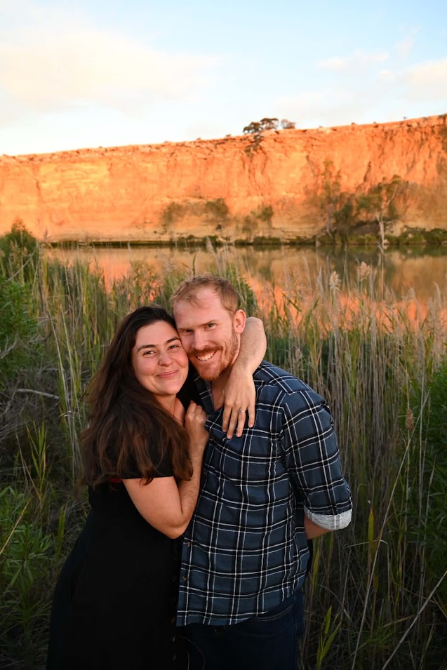Ellie and John smiling together among reeds at golden hour