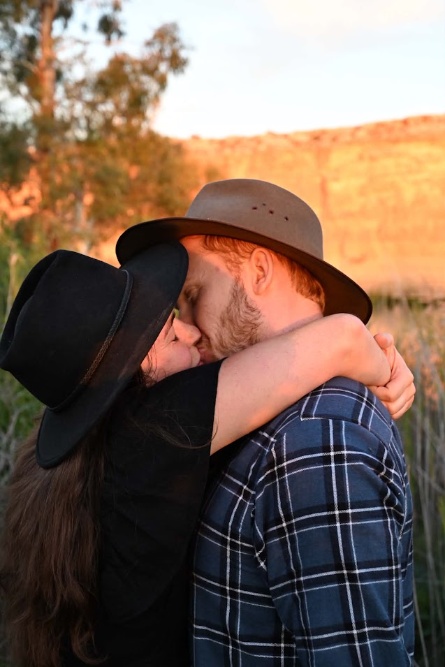 Ellie and John in wide-brimmed hats, foreheads together