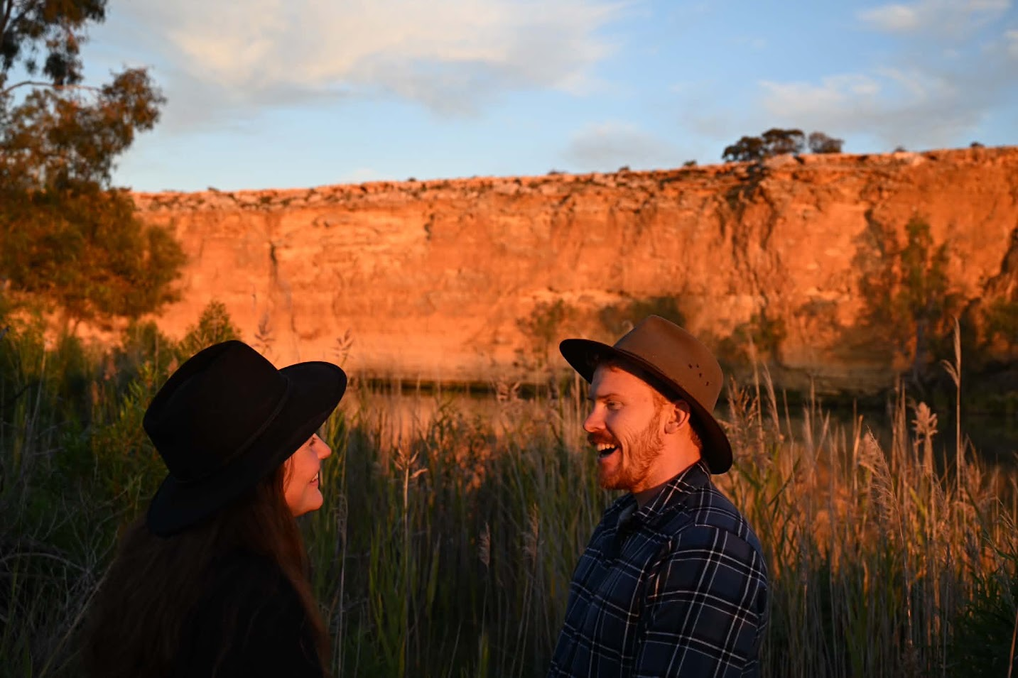 Ellie and John laughing together in front of a sunlit cliff