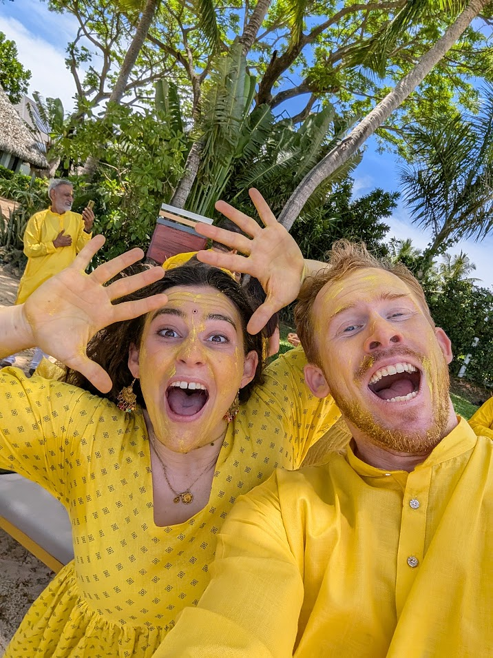 Ellie and John covered in yellow turmeric at a Haldi celebration